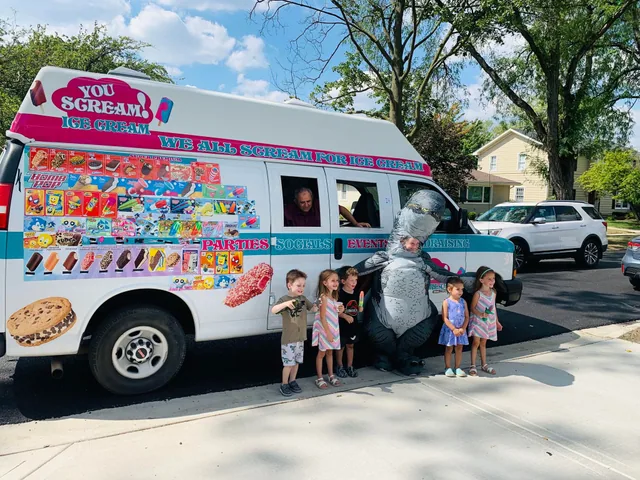 Children and a costumed mascot gathered at the ice cream truck window during a summer party
