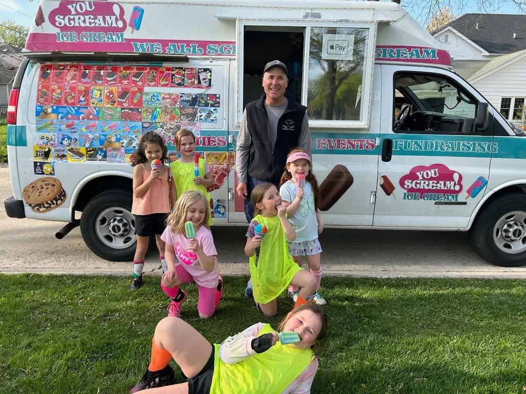 The owner leaning out of the truck window handing treats to a group of children on a sunny afternoon